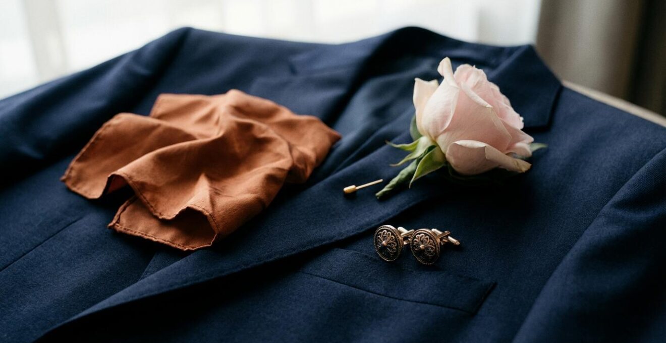 Pochette soie cuivrée et boutonnière florale disposées sur costume bleu marine