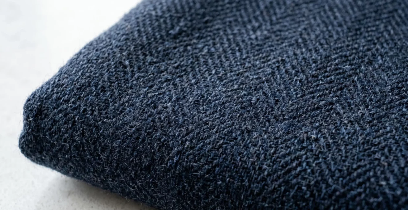 Gros plan sur la texture d'un tissu de laine premium révélant la finesse de l'armure et la profondeur de la matière